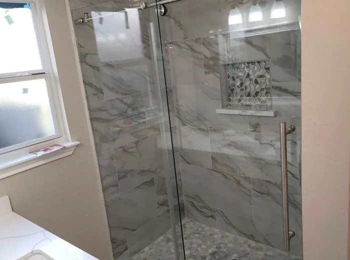 Completed bathroom remodel with a frameless sliding glass shower door and marble tile