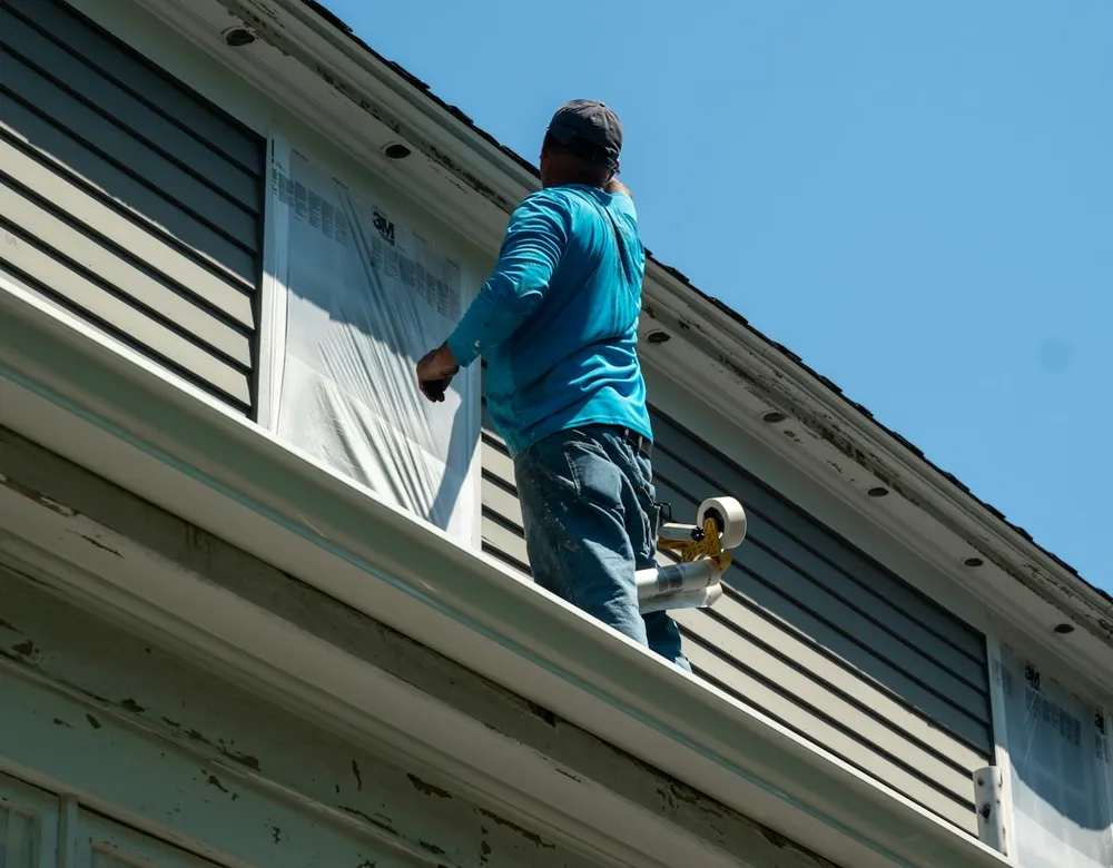Painter masking a window with plastic film before painting